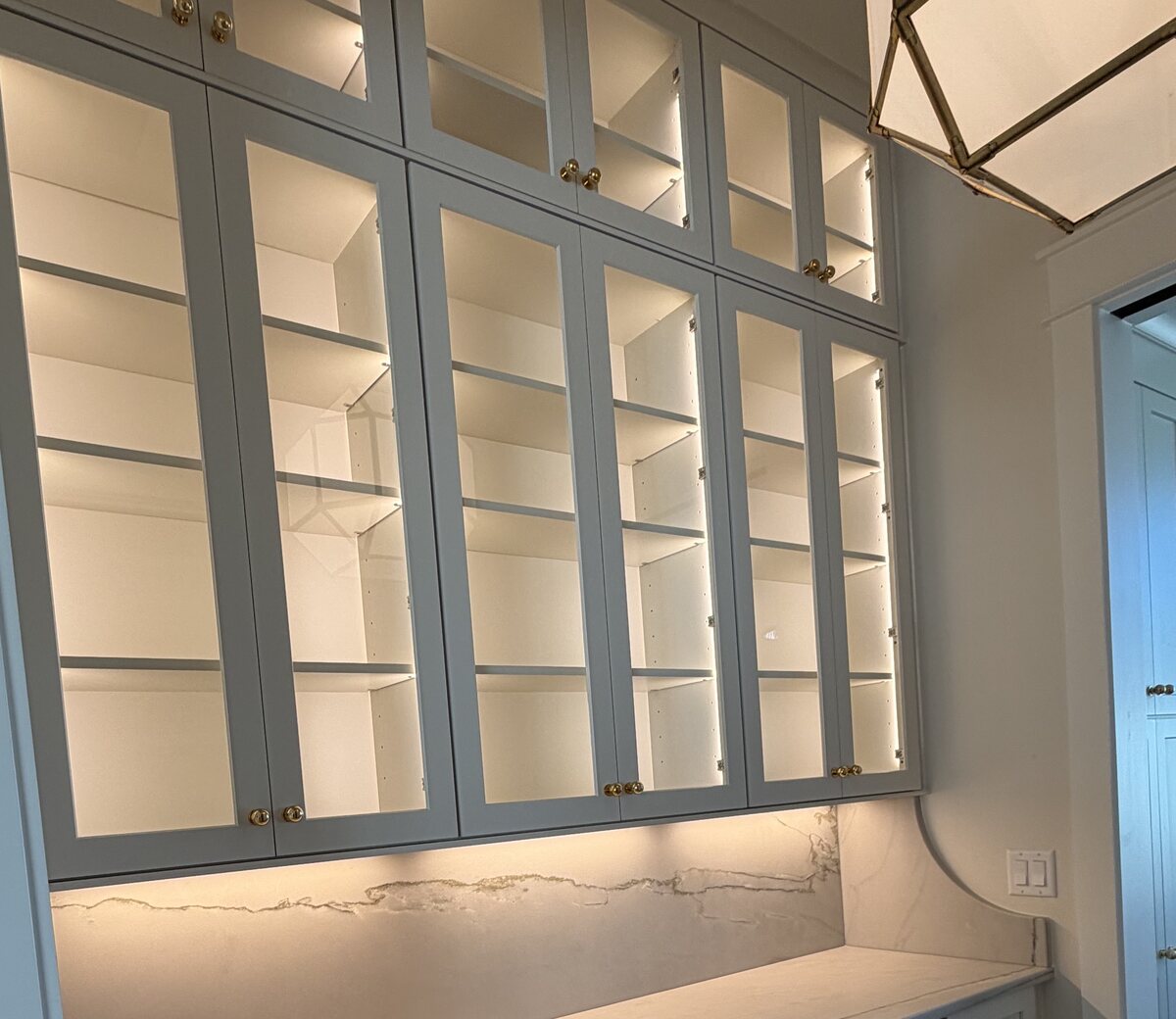 Detail of glass-front cabinet doors with brass knobs and lit interior shelving