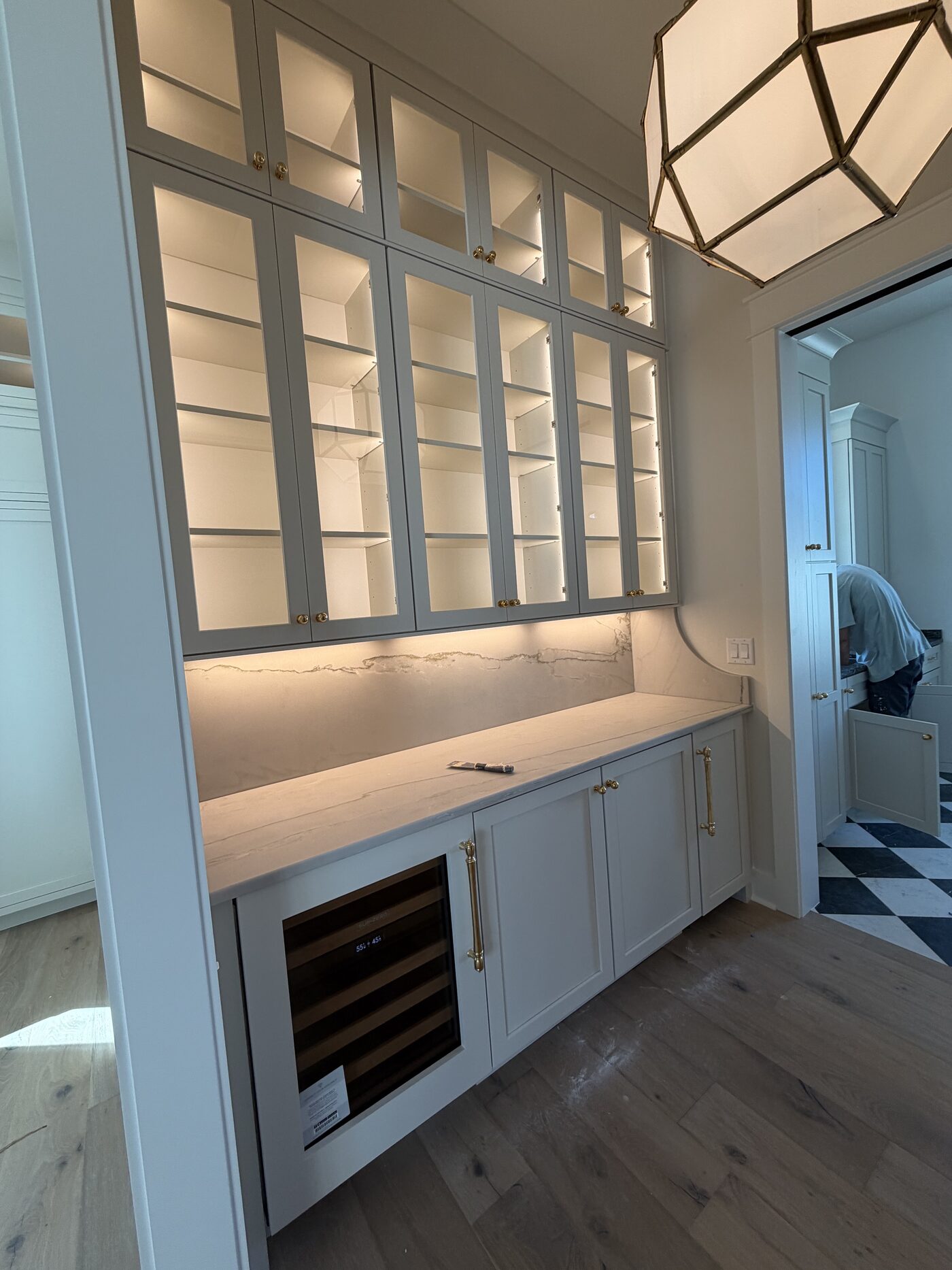 Butler's pantry with lit glass-front cabinets, quartz counter and backsplash, and an under-counter wine refrigerator