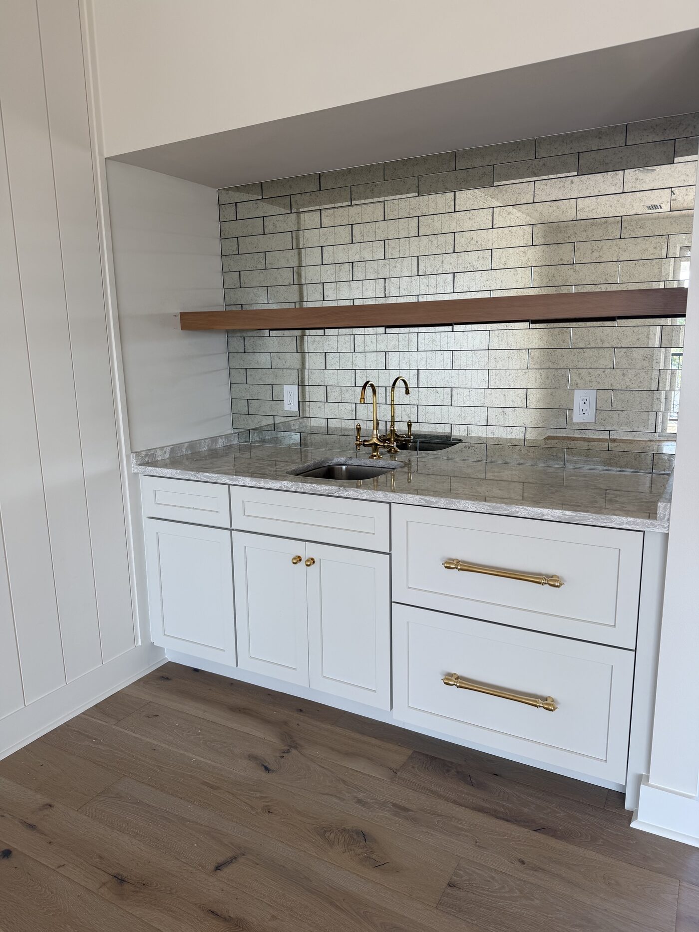 Wet bar with antique mirrored tile, a walnut floating shelf, granite counter and brass bridge faucet